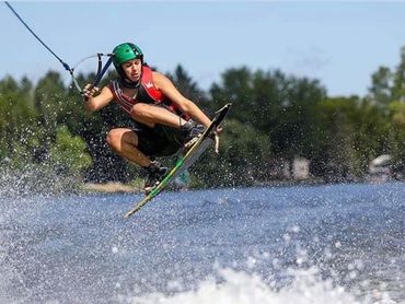 Wakeboarder performing a jump over water with a green helmet.