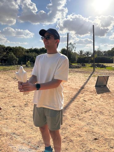 Young man holding a white dove outdoors on a sunny day.