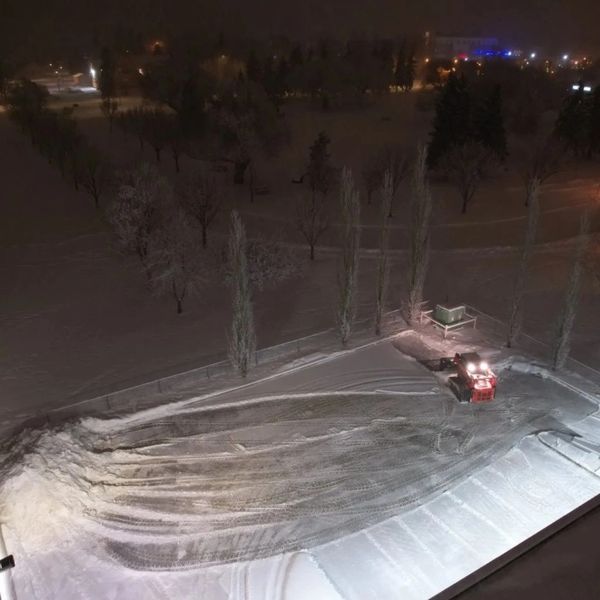 Snow plow clearing a large snowy area at night with lights on.