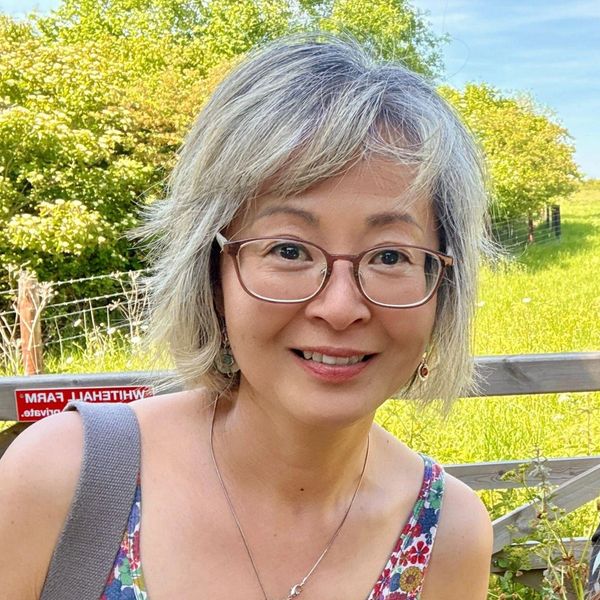 Smiling woman with gray hair and glasses outdoors on a sunny day.