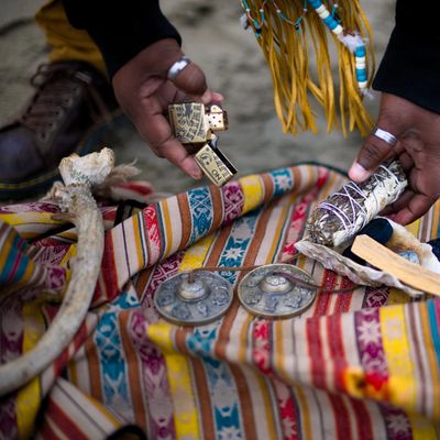 Hands holding a lighter and smudge stick over a colorful patterned cloth with ritual items.