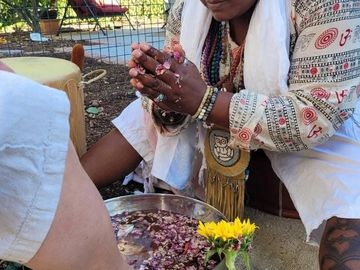Person performing a ritual with flower petals and a bowl of water.