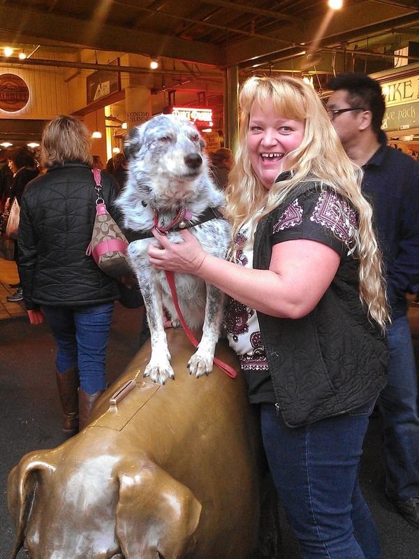 Woman holding dog on bronze dog statue.