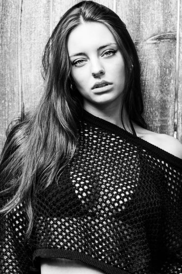 Black and white portrait of a woman in a mesh top against a wooden background.