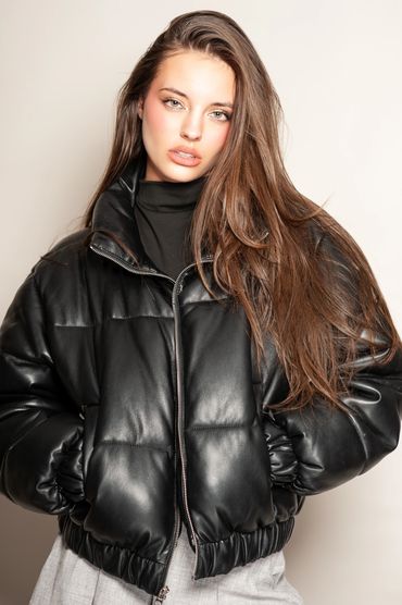 Young woman in a black leather puffer jacket with long brown hair.