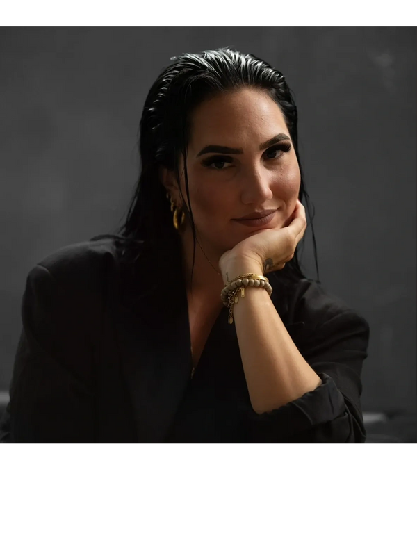 Portrait of a confident woman with slicked-back hair and gold jewelry.