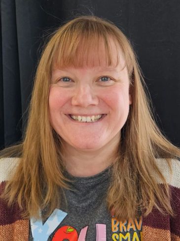 Smiling woman with red hair and bangs in a casual shirt and cardigan.