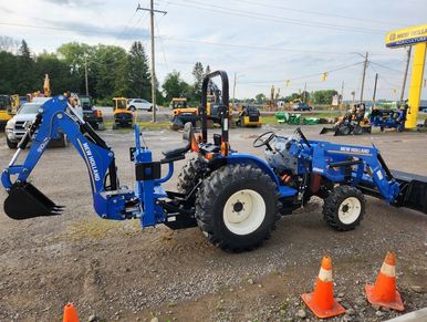 Blue New Holland tractor with backhoe and loader attachments in an equipment yard.