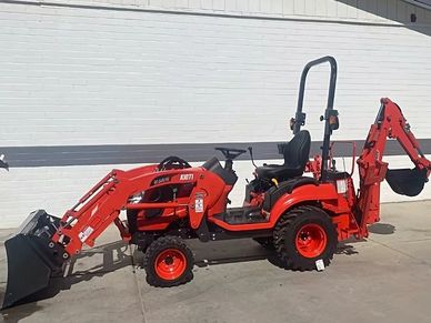 A bright orange Kioti compact tractor with front loader and backhoe attachments parked on concrete.