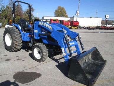 A blue New Holland tractor with a front loader attachment parked on a paved lot.