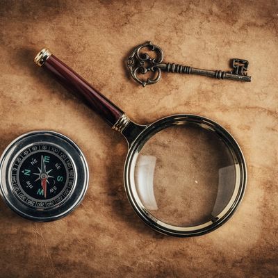 Antique parchment with a key, magnifying glass and compass laid on it.