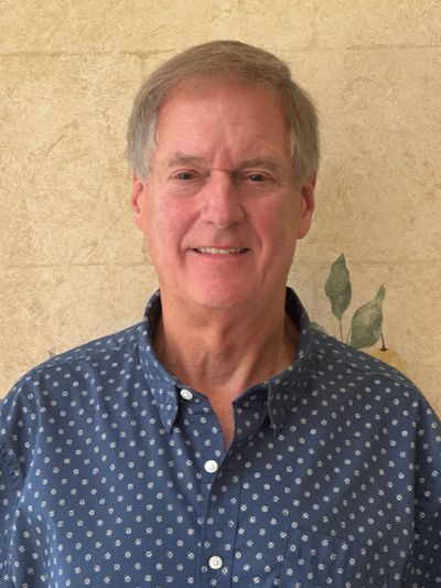 Smiling older man in a blue patterned shirt.