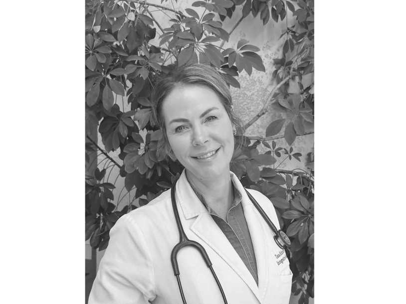 Smiling female doctor with stethoscope, standing outdoors.
