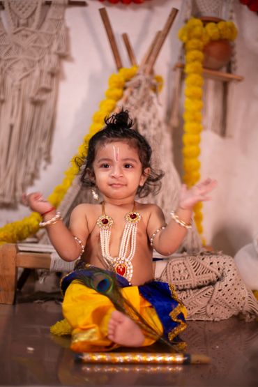 A baby dressed in traditional attire with jewelry and a peacock feather.