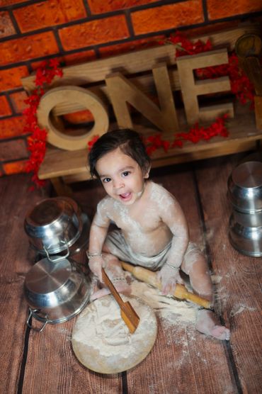 Happy baby playing with flour and kitchen utensils around.