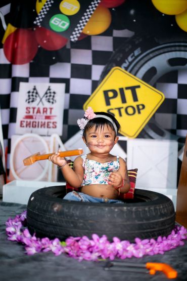 A smiling child plays inside a tire with a toy wrench in a racing-themed setting.