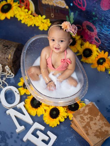 Smiling baby in a bubble bath surrounded by sunflowers and letters.