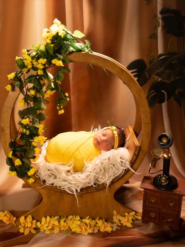 Newborn baby wrapped in yellow, resting in a wooden cradle adorned with yellow flowers.
