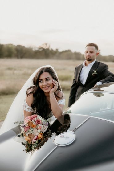 Bride and groom leaning on a car