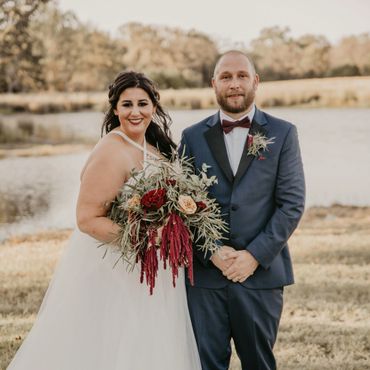 Bride and groom smiling and holding flowers in front of a lake