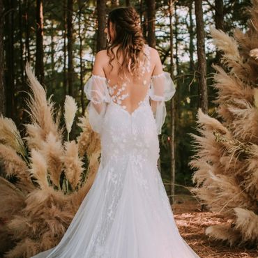 Bride facing away in front of pampas grass flower arrangements and woods