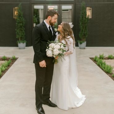 Bride and groom looking at each other and holding flowers in front of a building