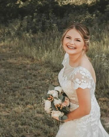 Bride smiling and holding flowers in a field