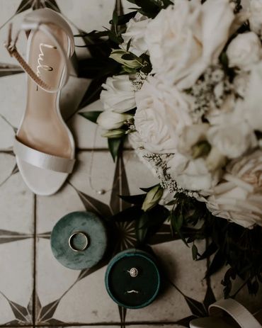 Shoe, flowers and wedding ring on a checkered floor.