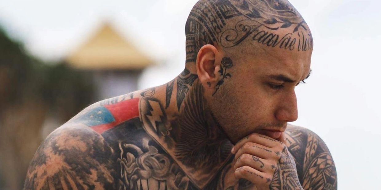 Thoughtful man with extensive tattoos on his head, neck, and chest.