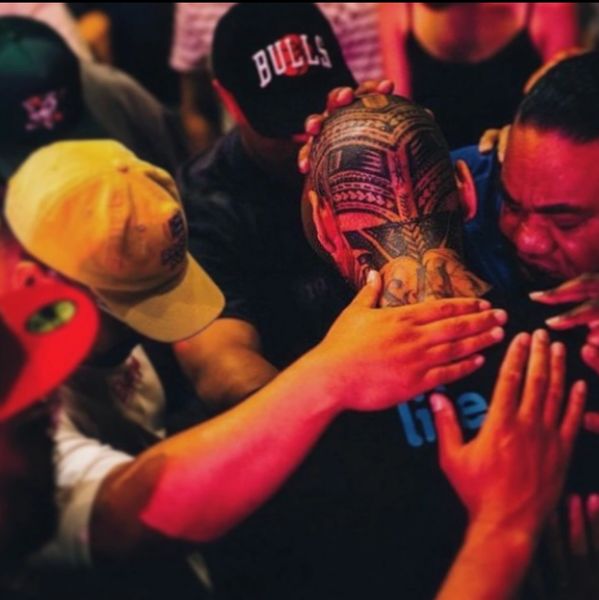 Group of men with hands on a tattooed head in a supportive gesture.