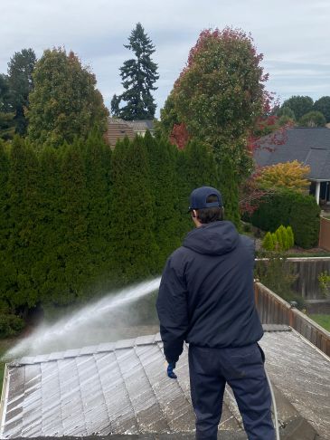 Man pressure washing a roof outdoors.