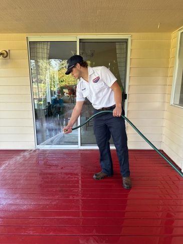 Man spraying water on a red deck with a hose.