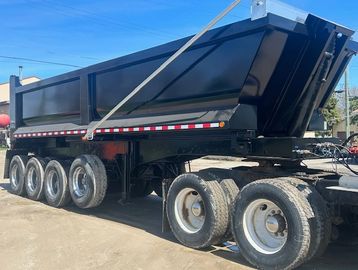 Black dump trailer with multiple wheels parked on dirt ground under clear blue sky.