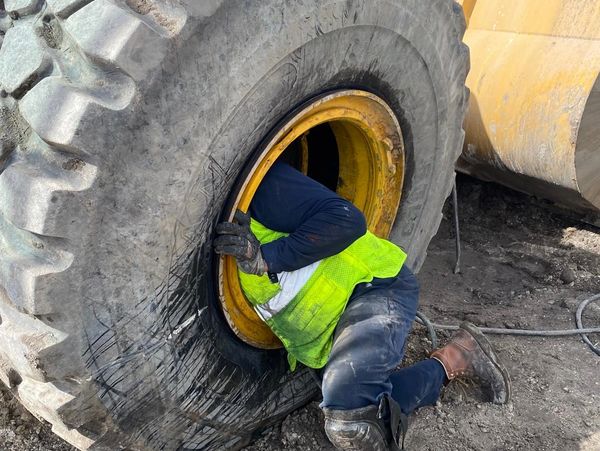 Worker inspecting or repairing a large industrial vehicle tire.