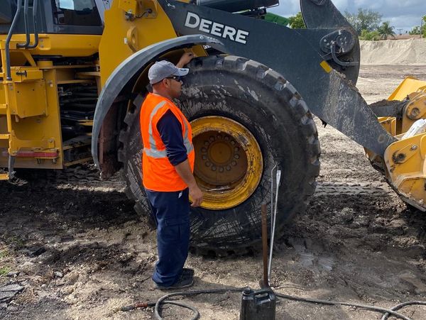 Worker inspecting a large tire on a Deere construction vehicle.