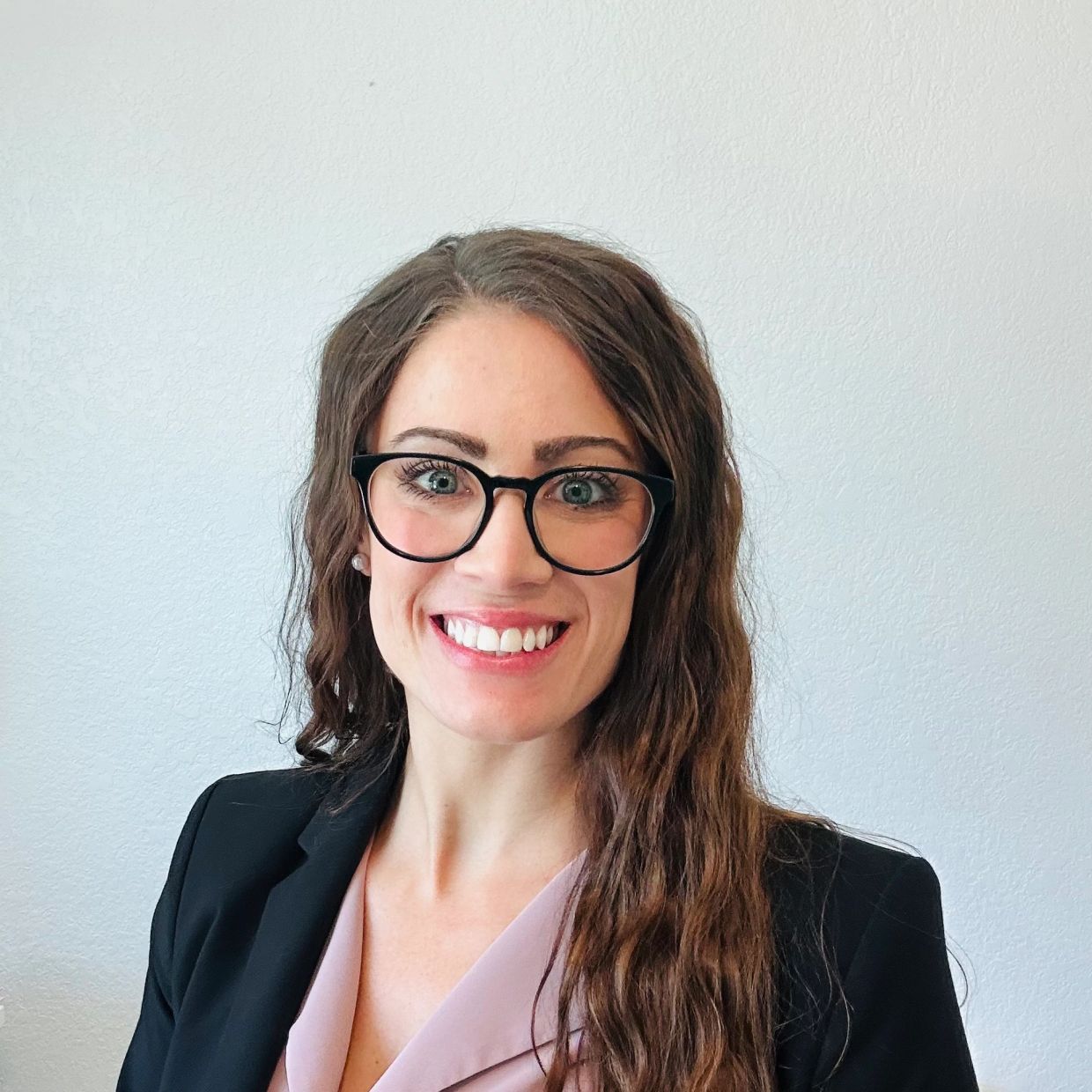 Smiling woman with glasses and long hair in business attire.