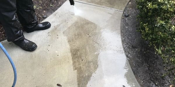 man wearing rubber boots power washing a cement sidewalk