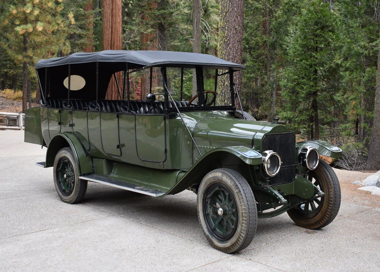 Vintage green open-top car parked on a forest road.