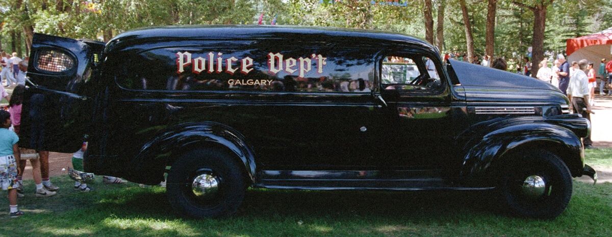 Vintage black Calgary Police Dept vehicle parked outdoors with open rear door.