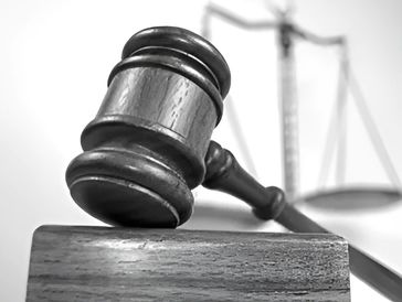 A close-up of a wooden gavel striking a block, with a blurred scale of justice in the background