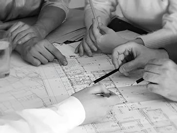 Several hands point and gesture over architectural blueprints during a collaborative