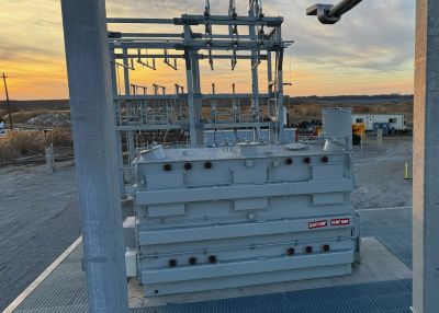 Electrical transformer at a power substation during sunset.