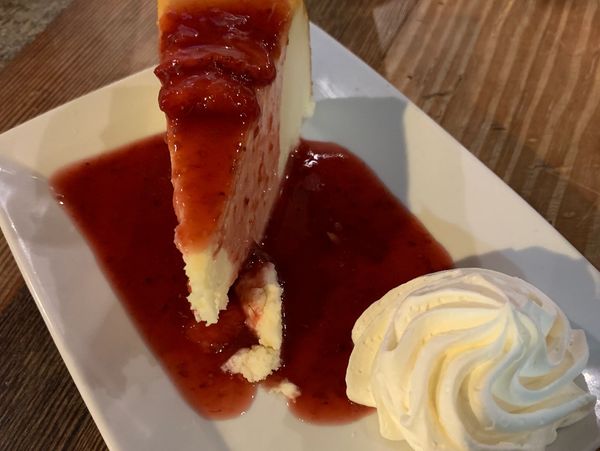 Cheesecake slice with strawberry sauce and whipped cream.