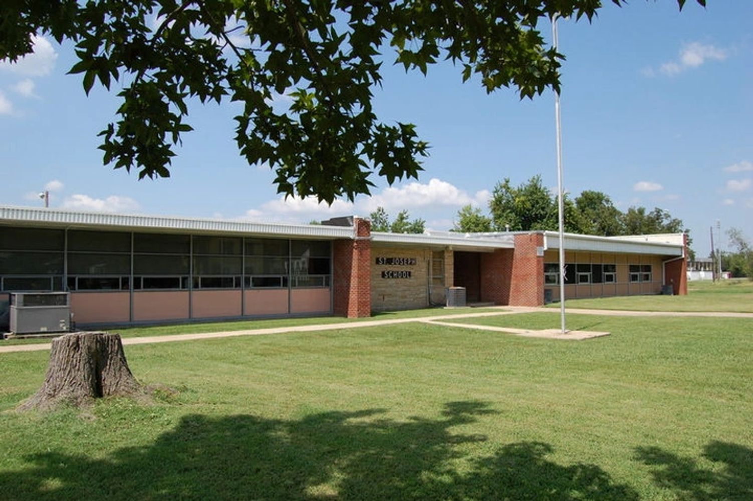 Exterior view of a single-story school building with a flagpole and tree shadows.