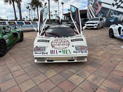 White sports car with upward-opening doors and multiple sponsor logos.
