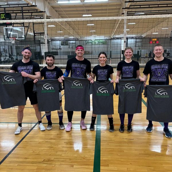 Six people holding championship t-shirts on a gym court.