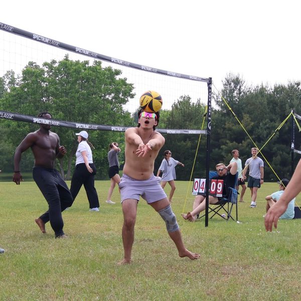 A man in sunglasses and knee brace plays volleyball outdoors on a grassy field.