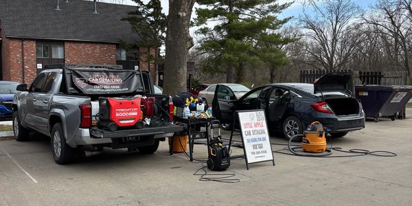 Multiple cars being detailed outdoors with equipment and a sign.