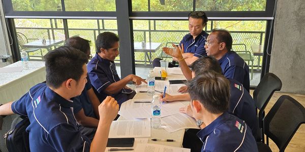 A group of men in uniforms collaborating around a table with documents and water bottles.