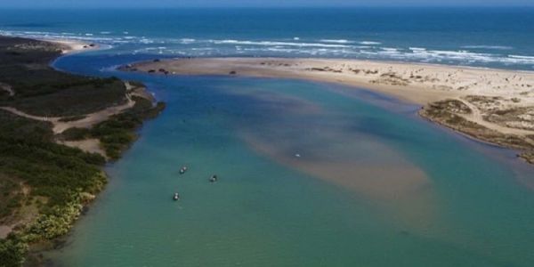 A river flowing into the ocean with small boats in the water.